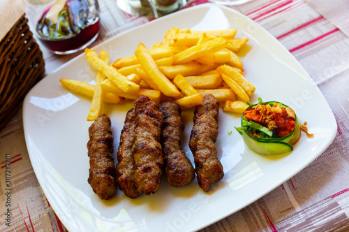 Grilled dish of minced meat with garnish of fried potatoes on white plate. Traditional Balkan cuisine, Cevapcici