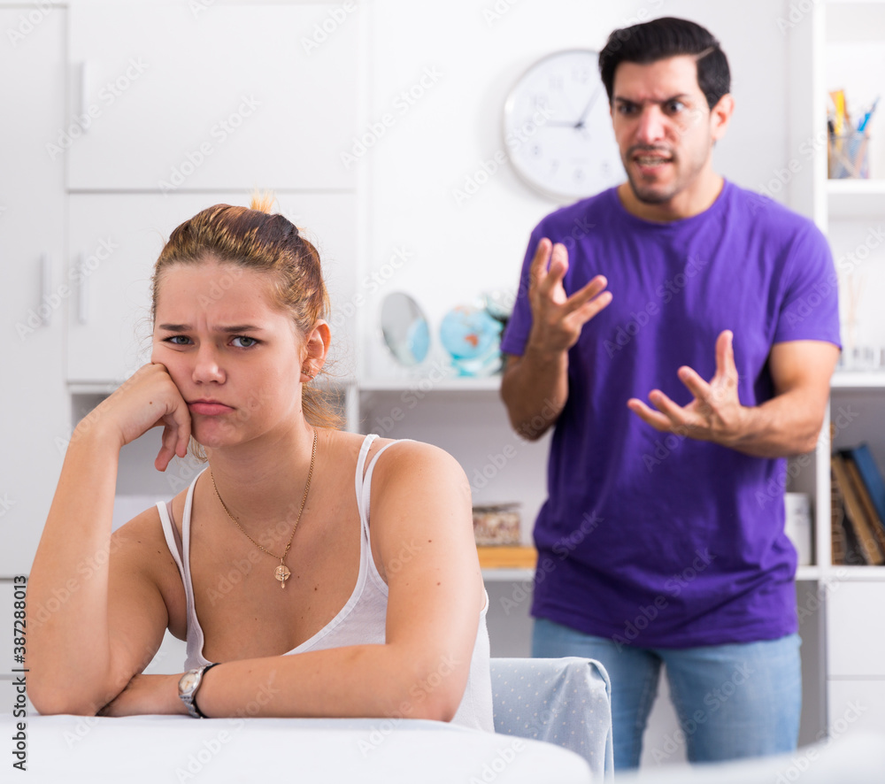 Obraz premium Upset young woman sitting at home table with disgruntled man behind