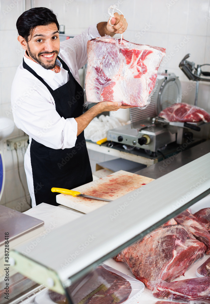 Satisfied smiling man butcher is demonstraiting meat in the market.