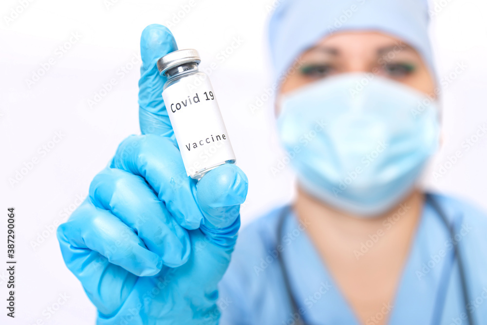 Vial with a vaccine against the virus in the hands of a doctor's face in blur. Vial with a vaccine against the virus in the hands of a doctor's face in blur.
