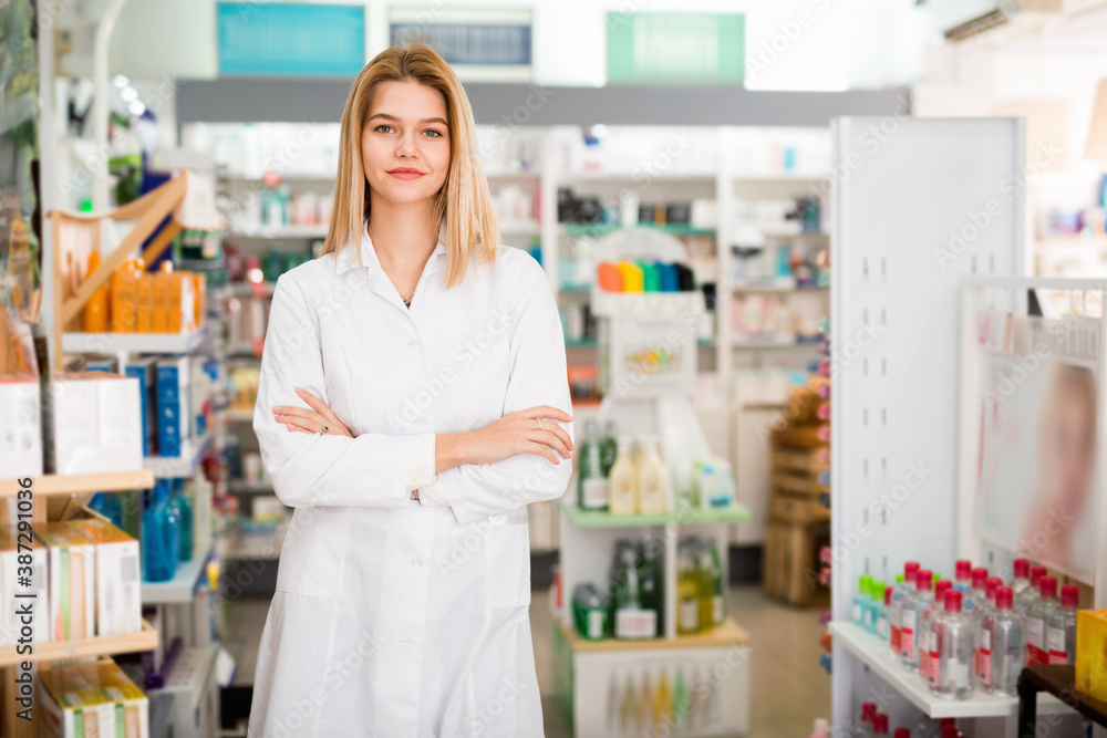 Portrait of young pleasant smiling cheerful female pharmacist in modern drugstore