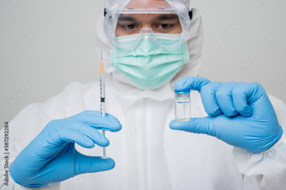 A portrait of virologist put on PPE suit holding syringe and vaccine bottle isolated on white background. Personal Protective Equipment Concept.. A portrait of virologist put on PPE suit holding syringe and vaccine bottle isolated on white background. Personal Protective Equipment Concept..