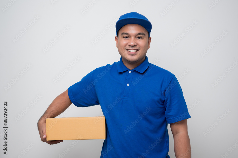 Young smiling asian delivery man in blue uniform holding box parcel cardboard on isolated white background. Young smiling asian delivery man in blue uniform holding box parcel cardboard on isolated white background.