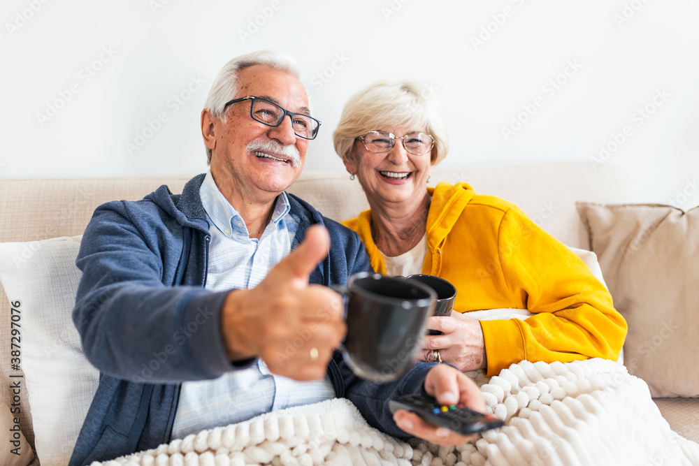 Senior couple sitting on the sofa,covered with blanket. feeling cozy, watching television. Elderly man showing thumb up Senior couple sitting on the sofa,covered with blanket. feeling cozy, watching television. Elderly man showing thumb up
