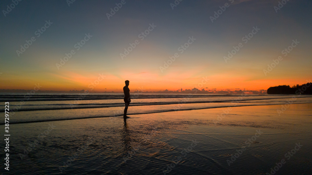 young man standing on the beach with a beautiful sunset