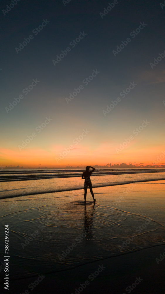 young woman standing on the beach with a beautiful sunset