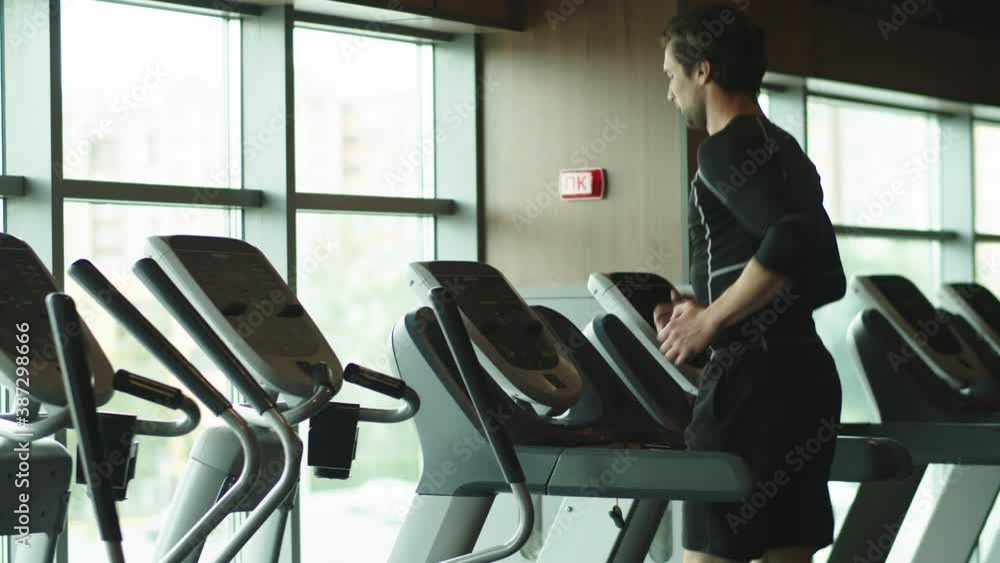 Sporty athlete warming up in sport club. Fit man running on treadmill at gym Sporty athlete warming up in sport club. Fit man running on treadmill at gym