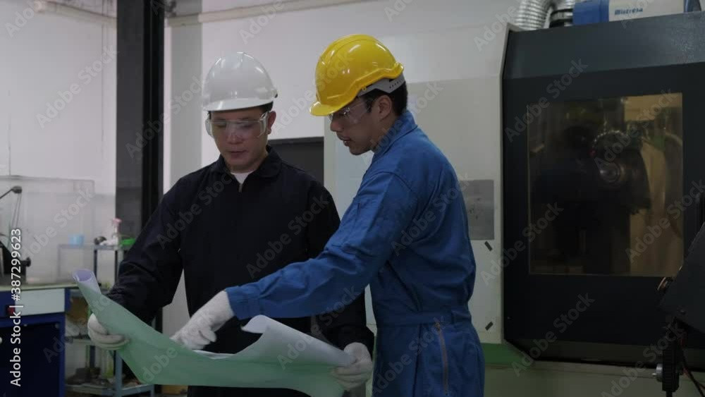 Two asian workers at heavy industry factory have conversation while looking at blueprint. Engineers explore and discuss project in heavy industry factory. Engineering and industrial concept. Two asian workers at heavy industry factory have conversation while looking at blueprint. Engineers explore and discuss project in heavy industry factory. Engineering and industrial concept.