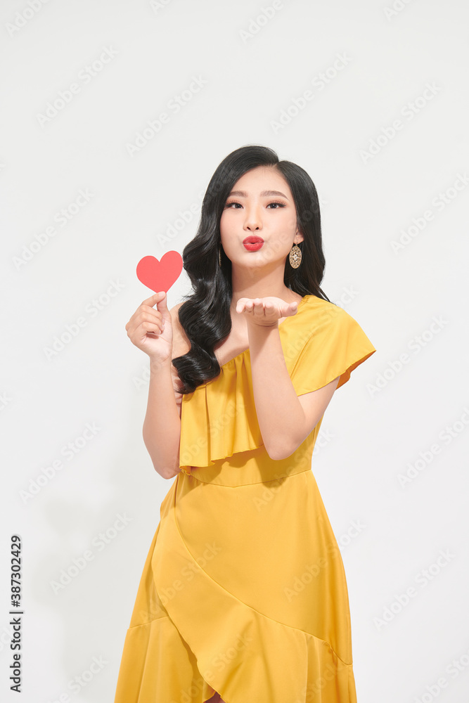 Young woman in red casual clothes sends air kiss, holds red heart Young woman in red casual clothes sends air kiss, holds red heart