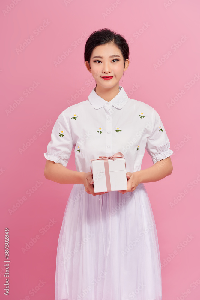 Portrait of a pretty smiling girl holding gift box and looking at camera isolated over pink background Portrait of a pretty smiling girl holding gift box and looking at camera isolated over pink background