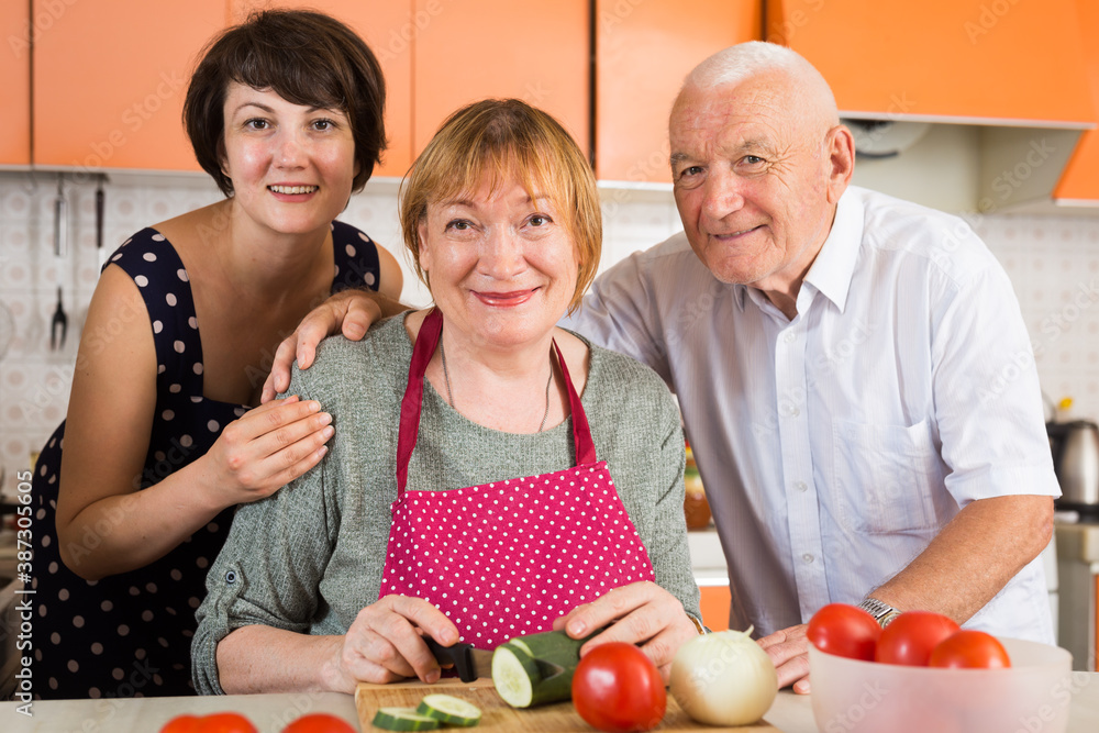 Happy elderly man and woman and their daughter making dinner together in kitchen