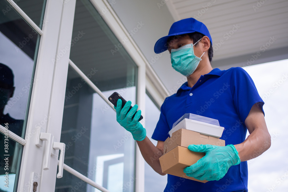 Male food delivery worker in a blue uniform wearing a mask and gloves is delivering food to the customer to the doorstep. The staff sends food to customers from order food online.
