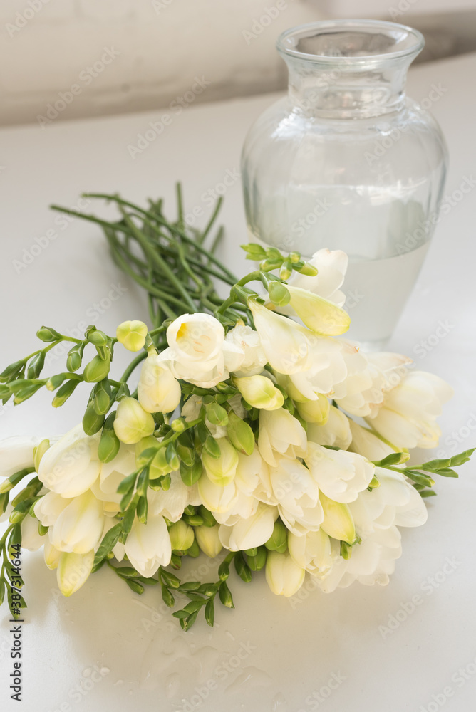 Vertical close up of white freesia flowers next to glass vase (selective focus)