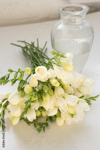 Vertical close up of white freesia flowers next to glass vase  selective focus 