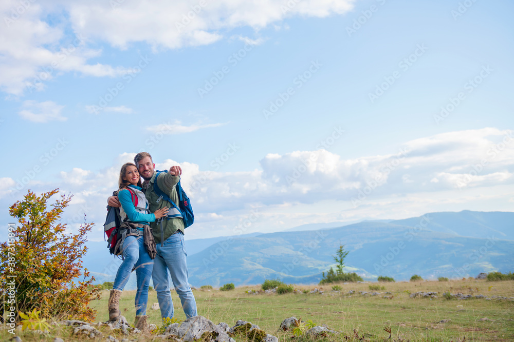 Two hikers with backpack standing on top of a mountain and look