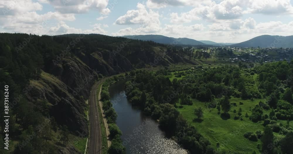 Empty railways under the rock near mountain river / dangerous part of Railways in Ural Mountains. Aerial drone top down view at summer sunny day. Empty railways under the rock near mountain river / dangerous part of Railways in Ural Mountains. Aerial drone top down view at summer sunny day.