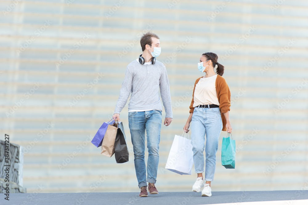 Shopping during Coronavirus pandemic concept. A young couple chatting and walking while holding their shopping bags. Shopping during Coronavirus pandemic concept. A young couple chatting and walking while holding their shopping bags.