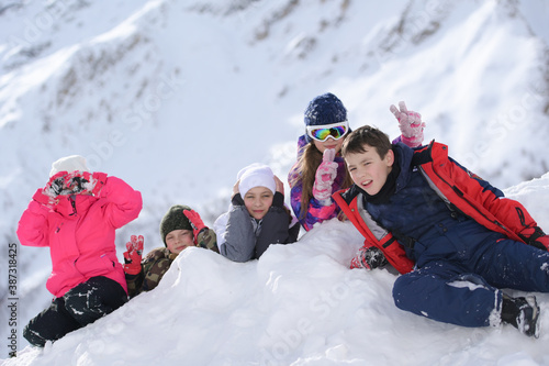 group of five little kids boys and girls in ski suit lying on white snow in alpine mountain resort leisure activity