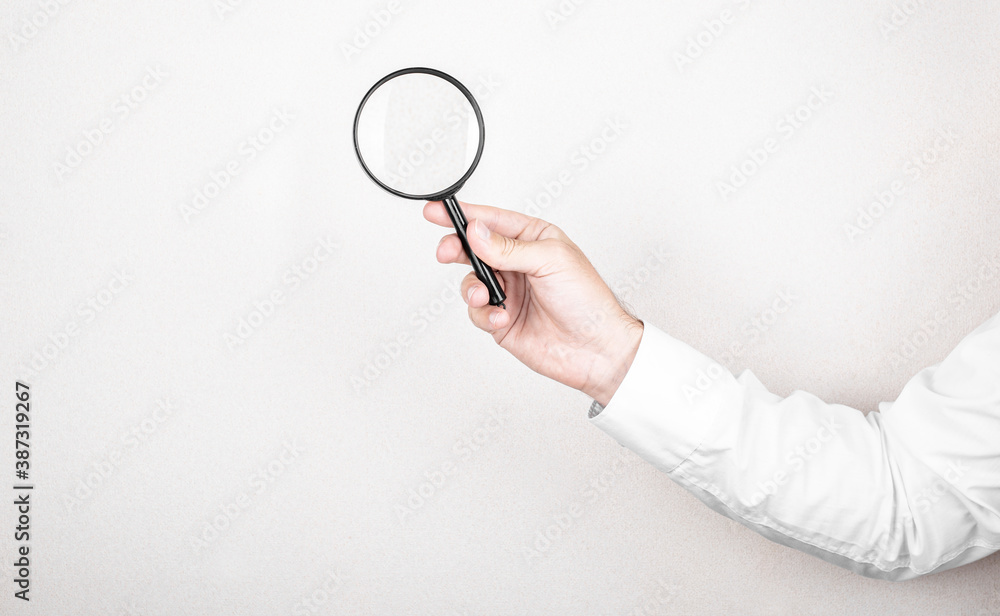 Man holds magnifying glass on wall background. Concept of search, recruitment and job search. Man holds magnifying glass on wall background. Concept of search, recruitment and job search.