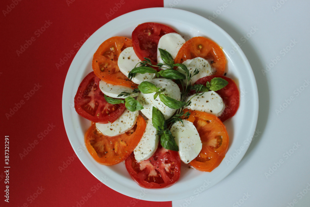 On a white and red background a plate with tomatoes and cheese On a white and red background a plate with tomatoes and cheese