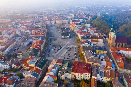 View from drone on large central square of Czech city of Jihlava overlooking medieval cathedrals, red steeple of Town Hall and modern shopping mall in fall morning..