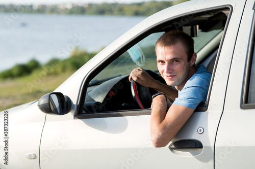 A young man looks out of the window of his car.