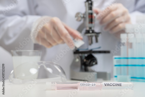 Doctor, laboratory assistant or microbiologist in protective gloves analyzes with microscope covid-19 vaccine on laboratory background. Backstage of scientific discovery. Healthcare concept.