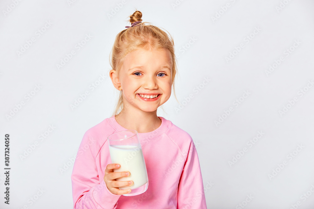 Cute little girl holding a large glass of milk. Kid 4-5 year old posing in studio on gray background Cute little girl holding a large glass of milk. Kid 4-5 year old posing in studio on gray background