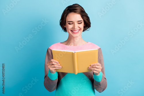 Photo portrait of happy smiling girl holding yellow book in two hands isolated on pastel light blue colored background