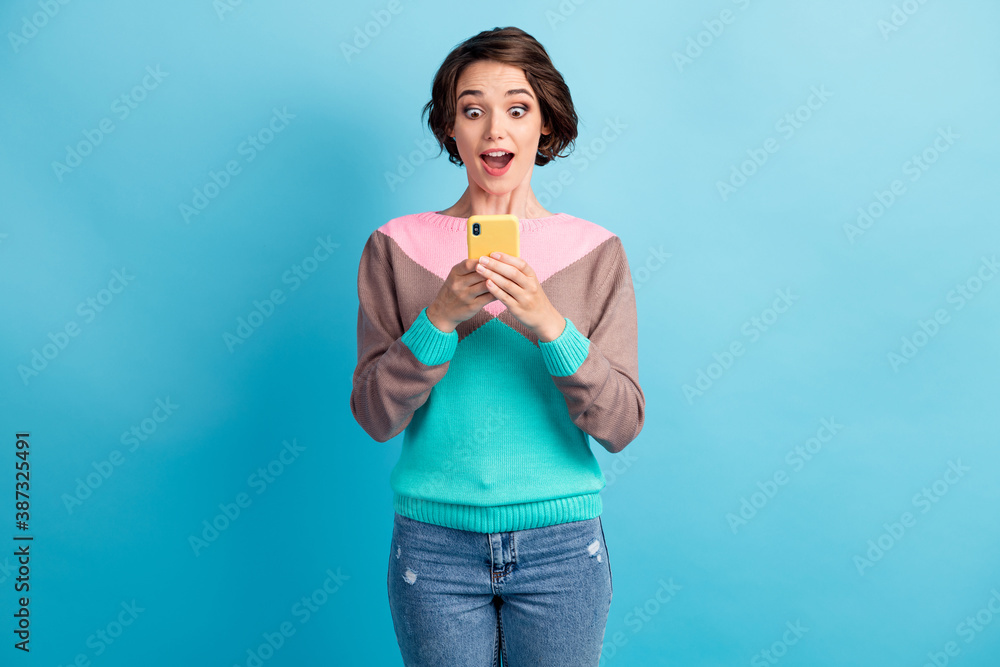 Photo portrait of surprised woman holding phone in two hands isolated on pastel light blue colored background Photo portrait of surprised woman holding phone in two hands isolated on pastel light blue colored background