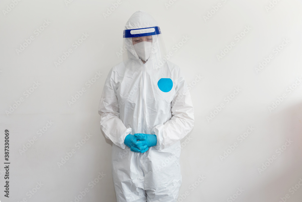 Doctor in white protective suit, face shield, medical mask and blue gloves stands and looks right to the camera. Fingers crossed. Epidemic, pandemic of coronavirus covid 19. Copy Space Doctor in white protective suit, face shield, medical mask and blue gloves stands and looks right to the camera. Fingers crossed. Epidemic, pandemic of coronavirus covid 19. Copy Space