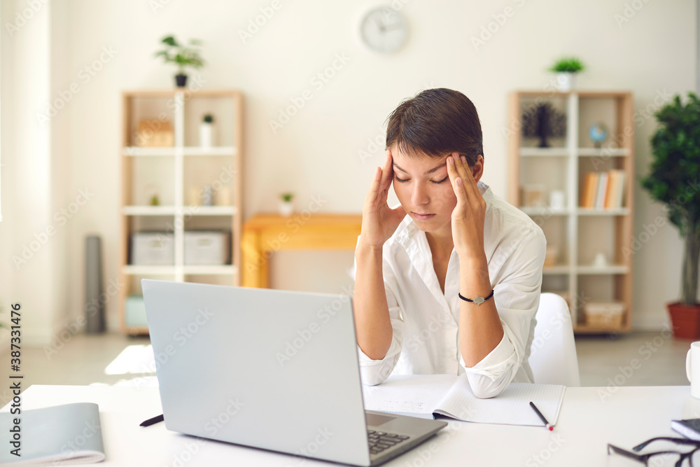 Tired woman with bad headache or blurry vision massaging temples sitting at desk with laptop Tired woman with bad headache or blurry vision massaging temples sitting at desk with laptop