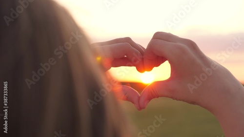 The girl made a beautiful heart from her finger in rays of the sun. healthy woman making heart shape with hands at sunset. Shining summer sun on your hands. healthy heart concept.