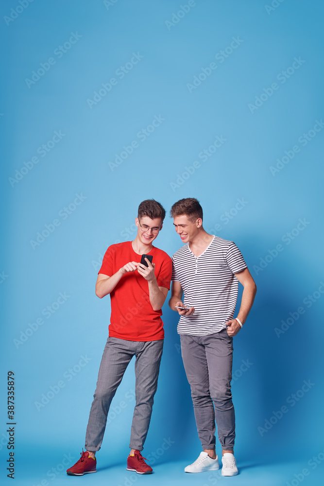 Youth and technology. Young happy friends using smartphone together. Blue background. Youth and technology. Young happy friends using smartphone together. Blue background.