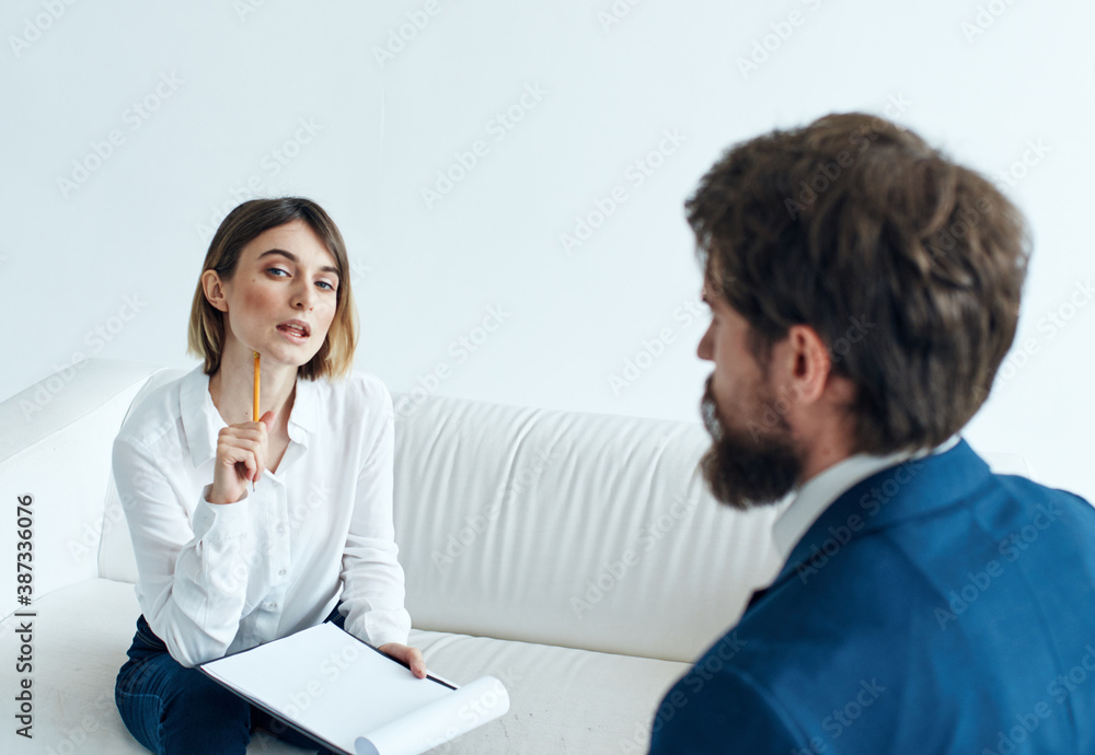 A man in a blue jacket and a beard talks to a woman on the sofa indoors
