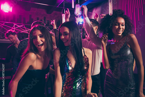 Photo portrait of cute attractive beautiful girls in front dancing together with guys in background at nightclub