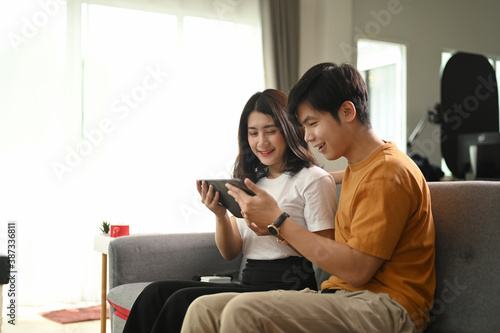 Cheerful happy couple using digital tablet together on sofa at home.