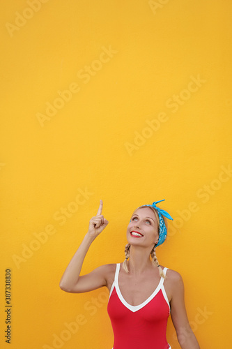 Your text here. Cheerful beautiful young woman pointing up while standing against yellow wall.