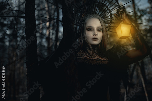 Portrait of woman in image of witch with glowing lamp in her hand in forest. photo
