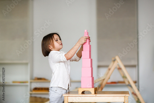 child girl playing with pink tower, developing sensory activities in montessori and earlier child development, kids independence photo