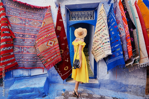 Colorful traveling by Morocco. Young woman in yellow dress walking in  medina of  blue city Chefchaouen.