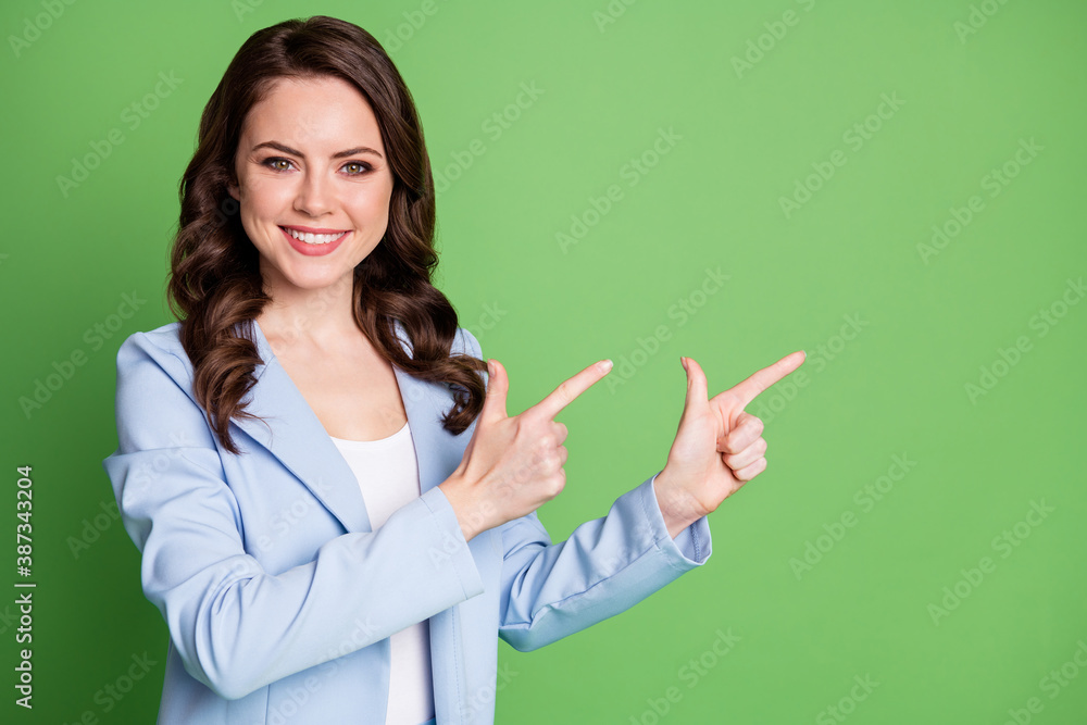 Photo of charming lady curly hairstyle direct fingers empty space toothy smile wear blue jacket isolated green color background Photo of charming lady curly hairstyle direct fingers empty space toothy smile wear blue jacket isolated green color background