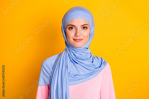 Close-up portrait of attractive cheery modest muslimah wearing blue hijab isolated over bright yellow color background photo