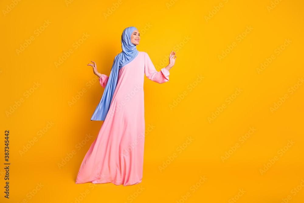Full length body size view of nice fashionable cheerful feminine muslimah walking copy space isolated on vivid yellow color background