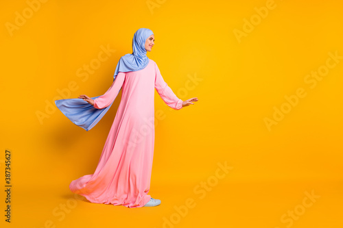Full length body size view of pretty cheerful muslimah wearing hijab dress looking aside walking copy space isolated shine yellow color background