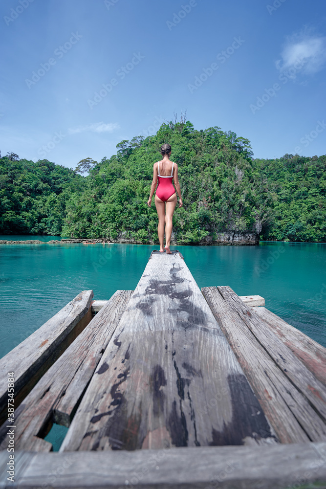 Vacation and activity. Young woman in swimsuit enjoying blue tropical lagoon view standing on wooden springboard. Siargao Island, Philippines.