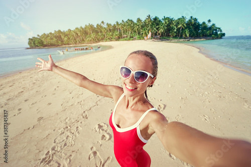 Traveling in Philippines. Pretty young woman in red swimsuit taking selfie on the white sand tropical beach.