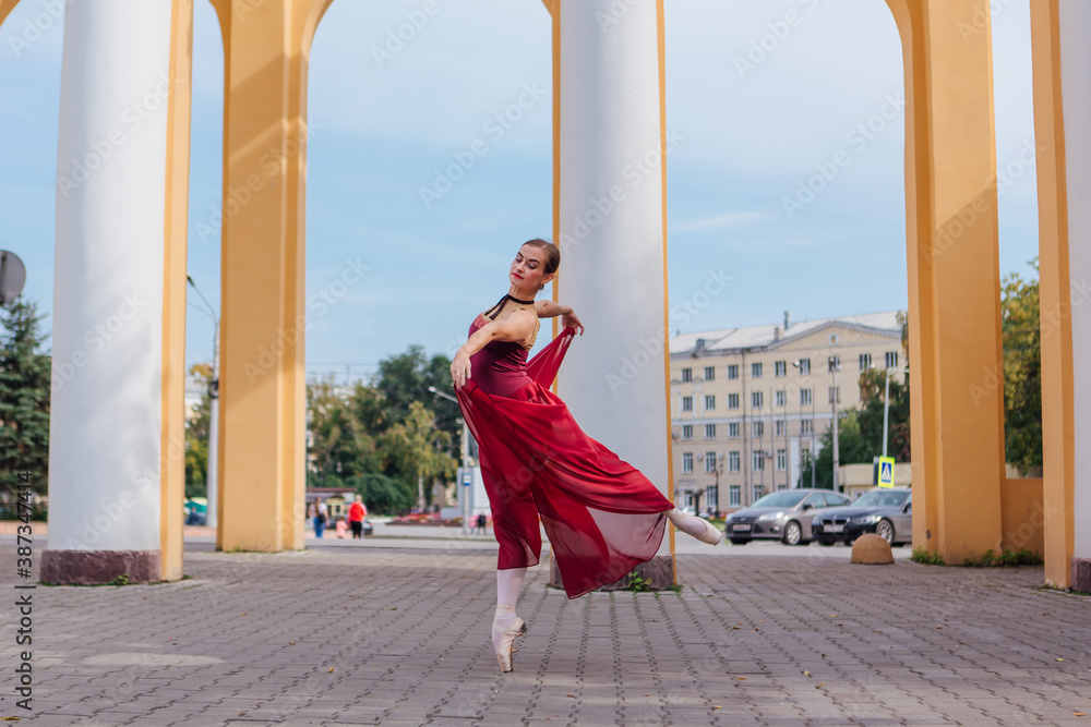 Woman ballerina in red ballet dress dancing in pointe shoes next to the old columns