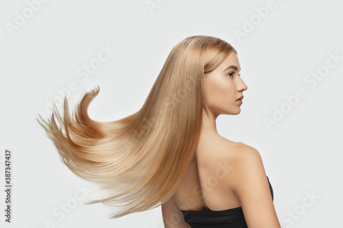 Wave. Beautiful model with long smooth, flying blonde hair on white studio background. Young caucasian model with well-kept skin and hair blowing on air. Concept of salon care, beauty, fashion. photo