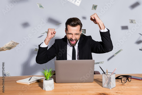 Photo of handsome crazy business guy notebook table usa bucks fall rich chief success startup income raise fists celebrate wear blazer shirt tie suit sit chair isolated grey background